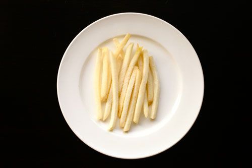 黑色背景的白色瓷盘里放着一些冷冻的麦当劳薯条。