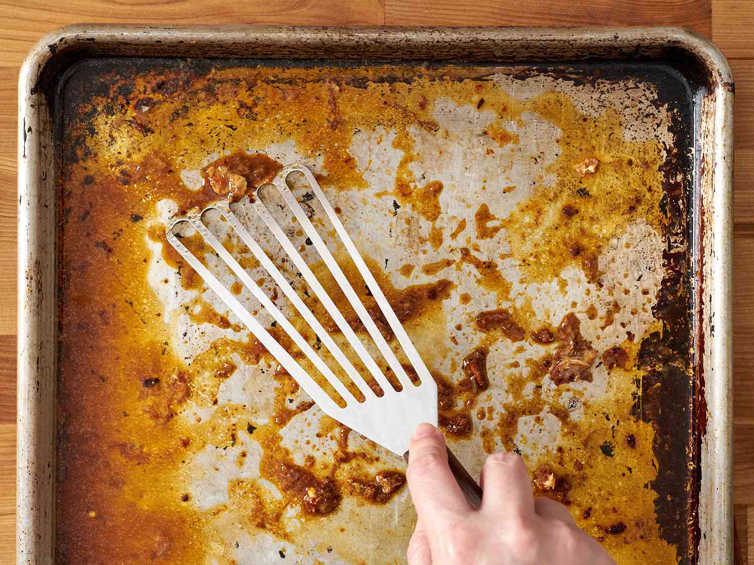 开槽刮刀从烤盘上刮下鸡油。
