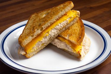 一个金枪鱼三明治三明治板,diago带领减少一半nally to make triangles; showing melted yellow American cheese slices on top of a creamy tuna salad and nicely toasted bread.