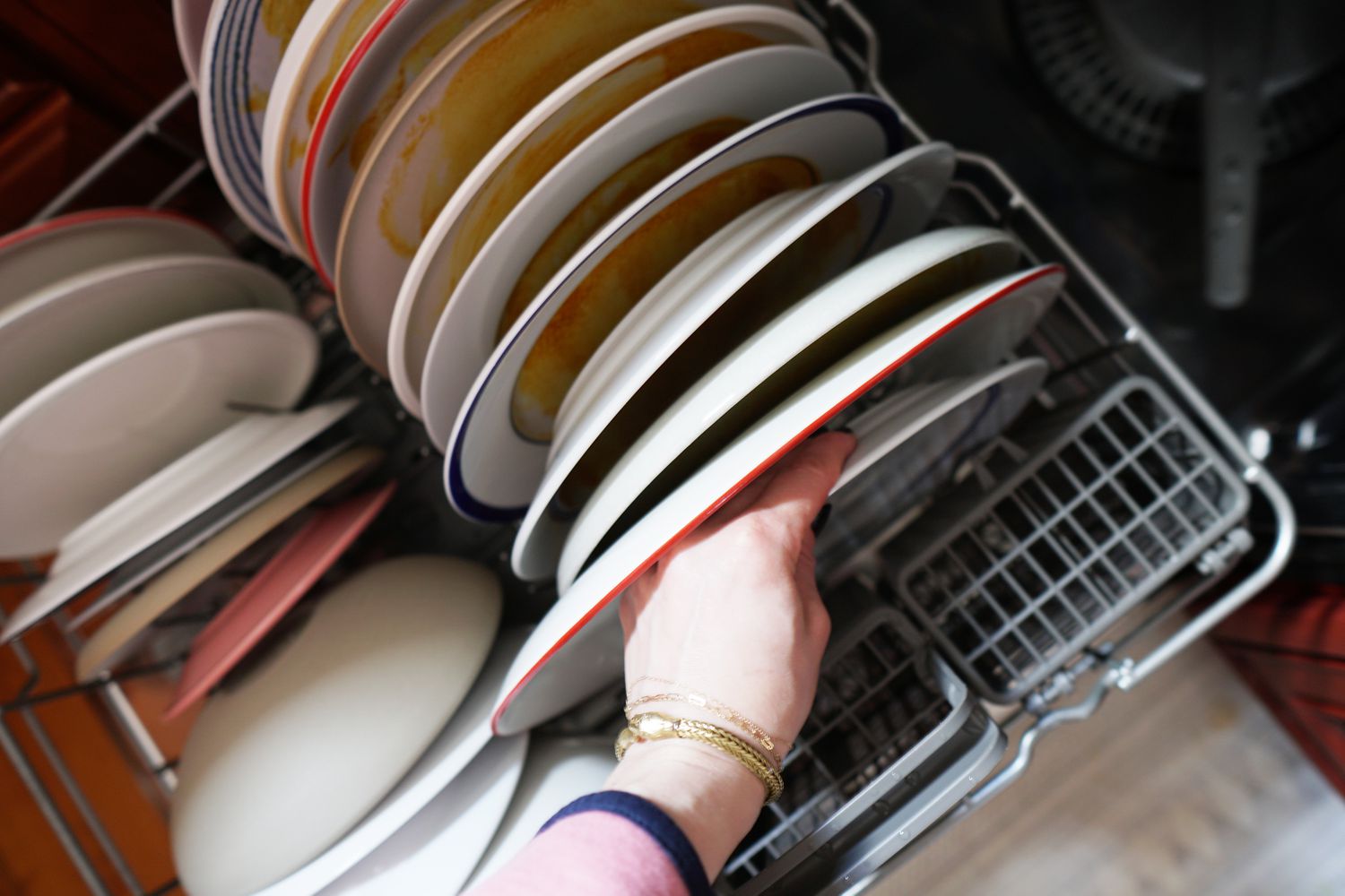 A person loading dinnerware into a dishwasher