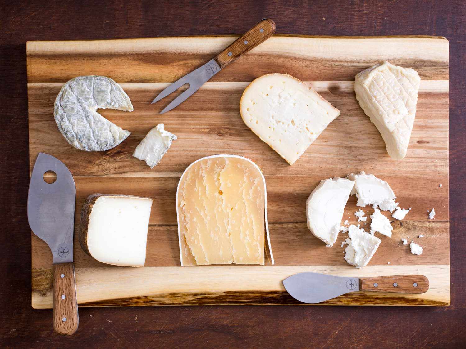 一组六种不同的奶酪放在砧板上，用三把奶酪刀。