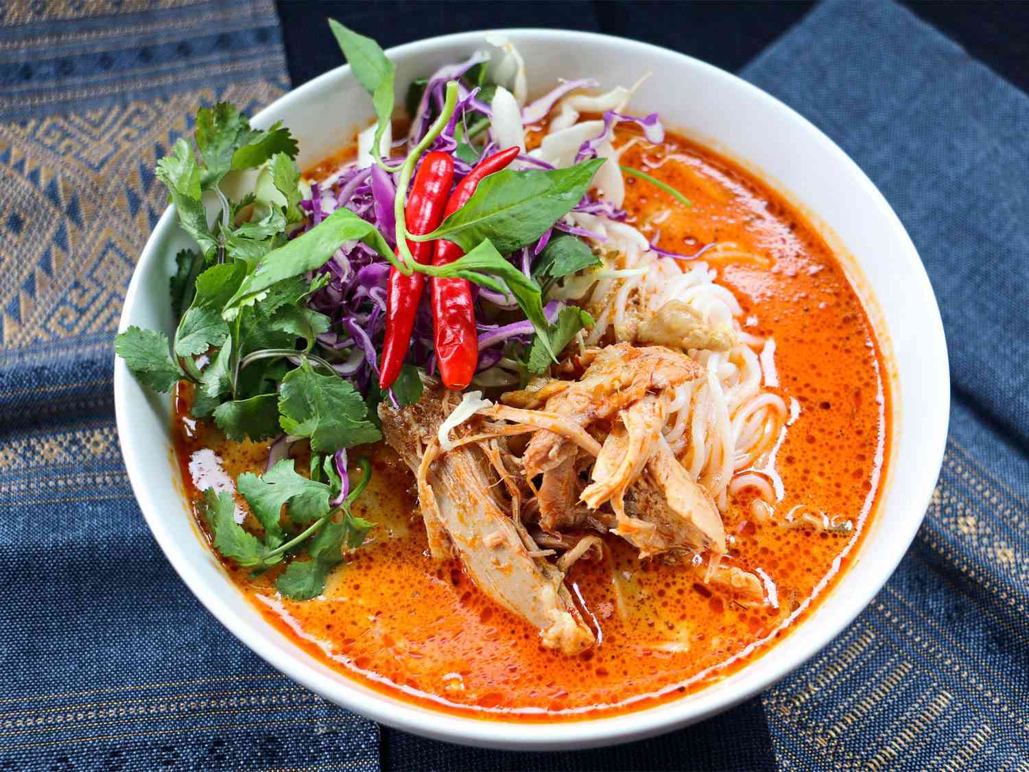 一碗khao poon:在鲜红的咖喱肉汤中发酵的粉丝面，配上肉、香草、红辣椒和紫色卷心菜