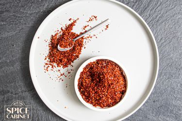 Overhead view of Aleppo Pepper on a plate on a grey background with an Aleppo Pepper logo in the lower left corner