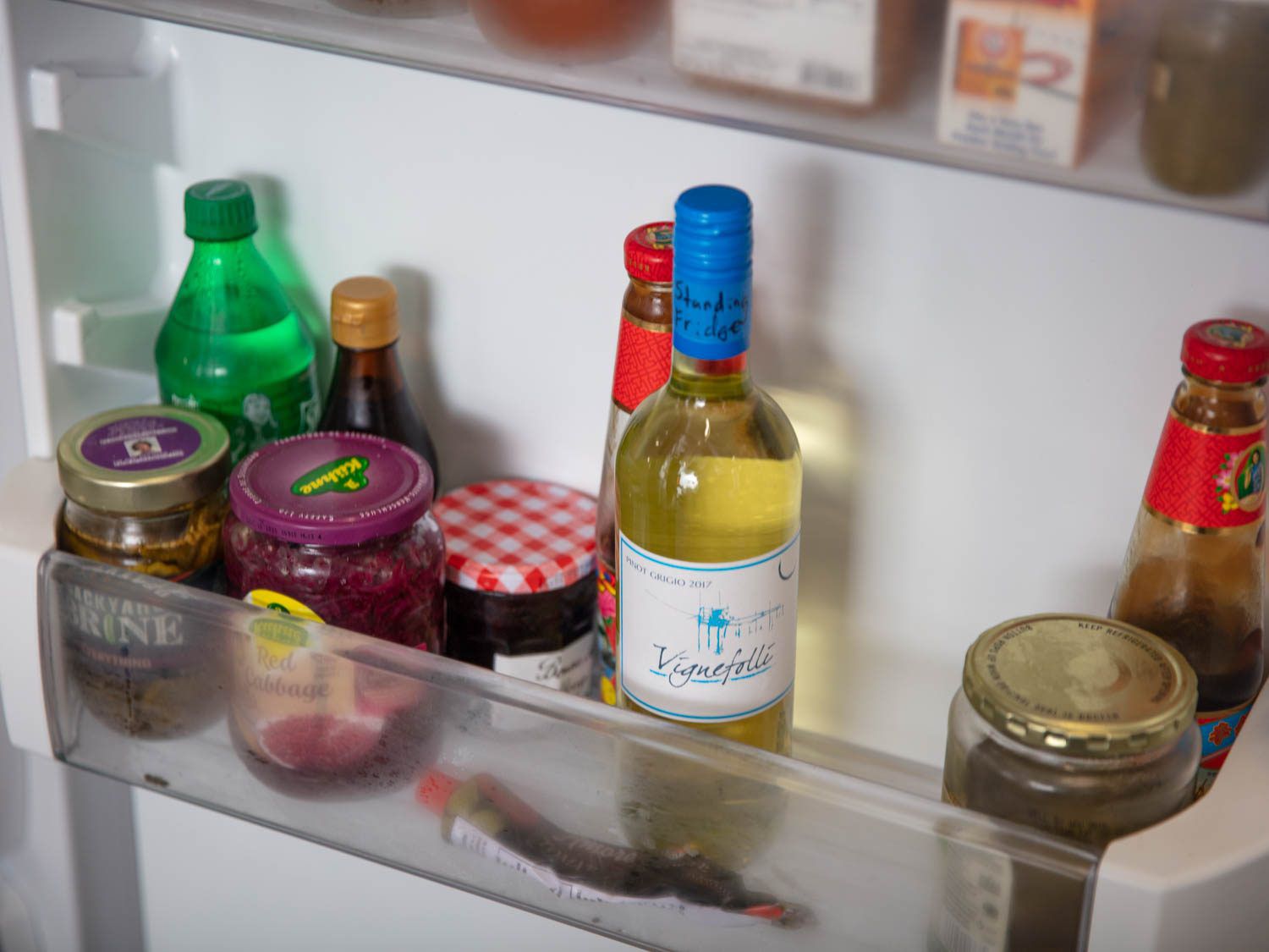 冰箱门上竖着一瓶白葡萄酒，旁边是一罐果酱和其他罐头食品