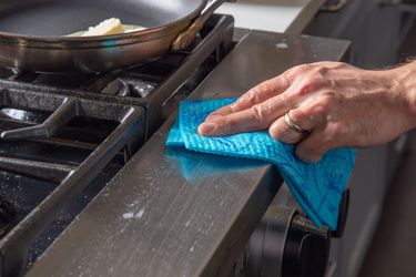Hand using a Swedish dishcloth to wipe down the front of a stove.