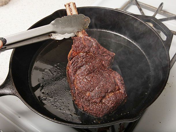 用金属夹子在煎锅里翻炒棕色的野牛肋眼牛排。