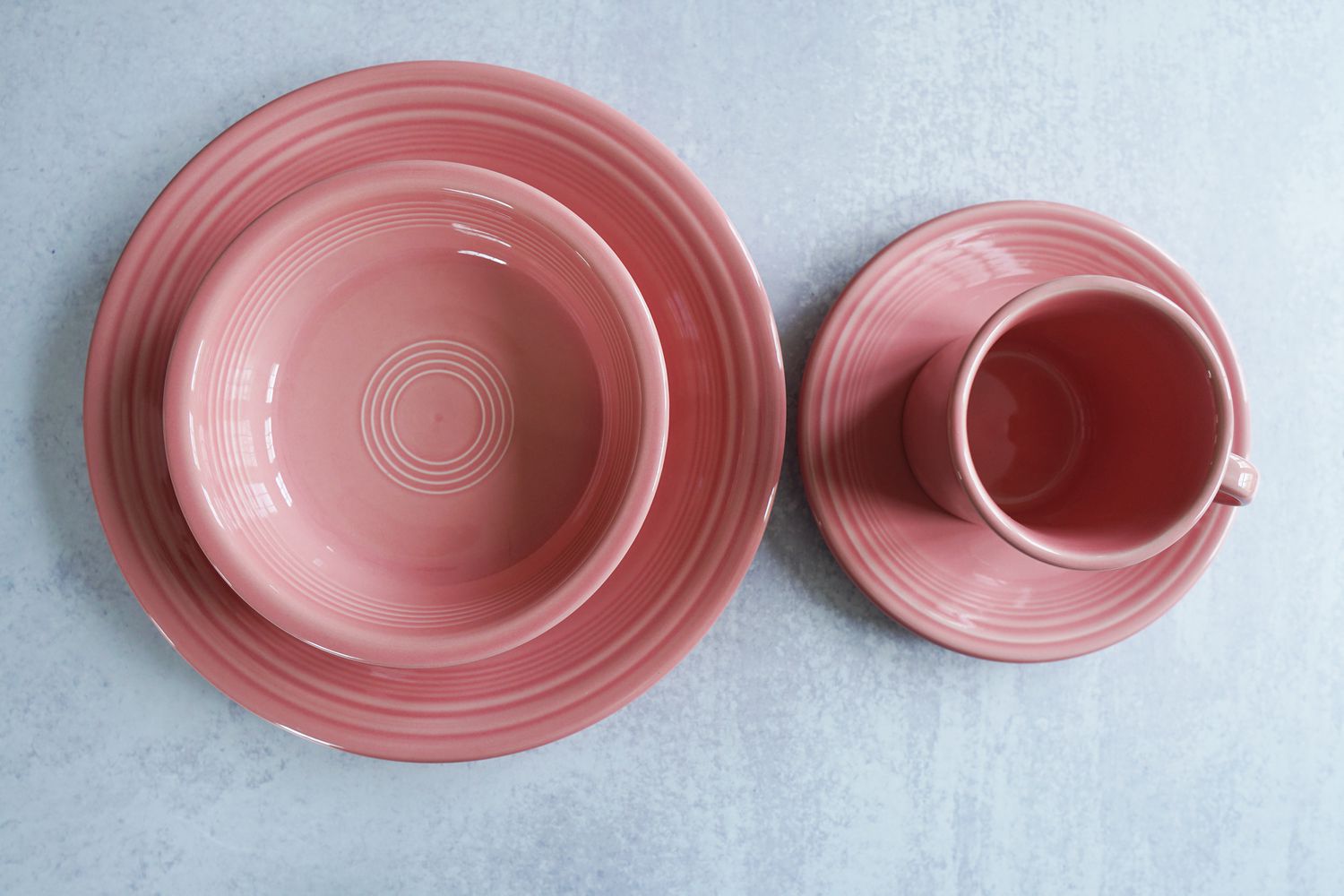 Two pink plates, a pink bowl, and a pink mug on a grey suface