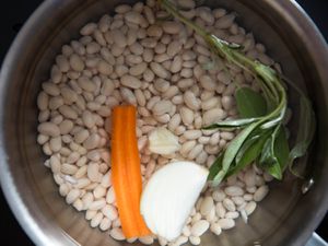 一个装满干豆、胡萝卜、蒜瓣、洋葱和一枝新鲜鼠尾草的罐子。