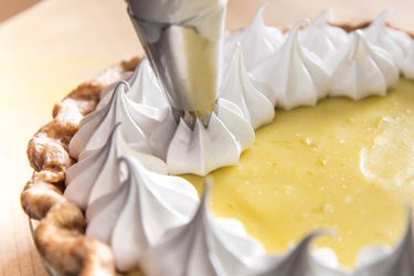 a piping bag piping meringue onto the filling of a fresh and creamy lime pie.
