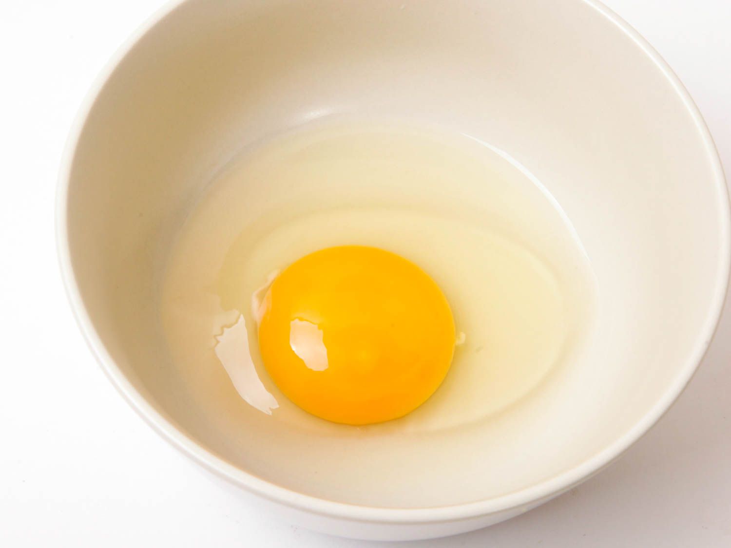 一个人在一个白色的碗里打碎了整个鸡蛋。gydF4y2Ba
