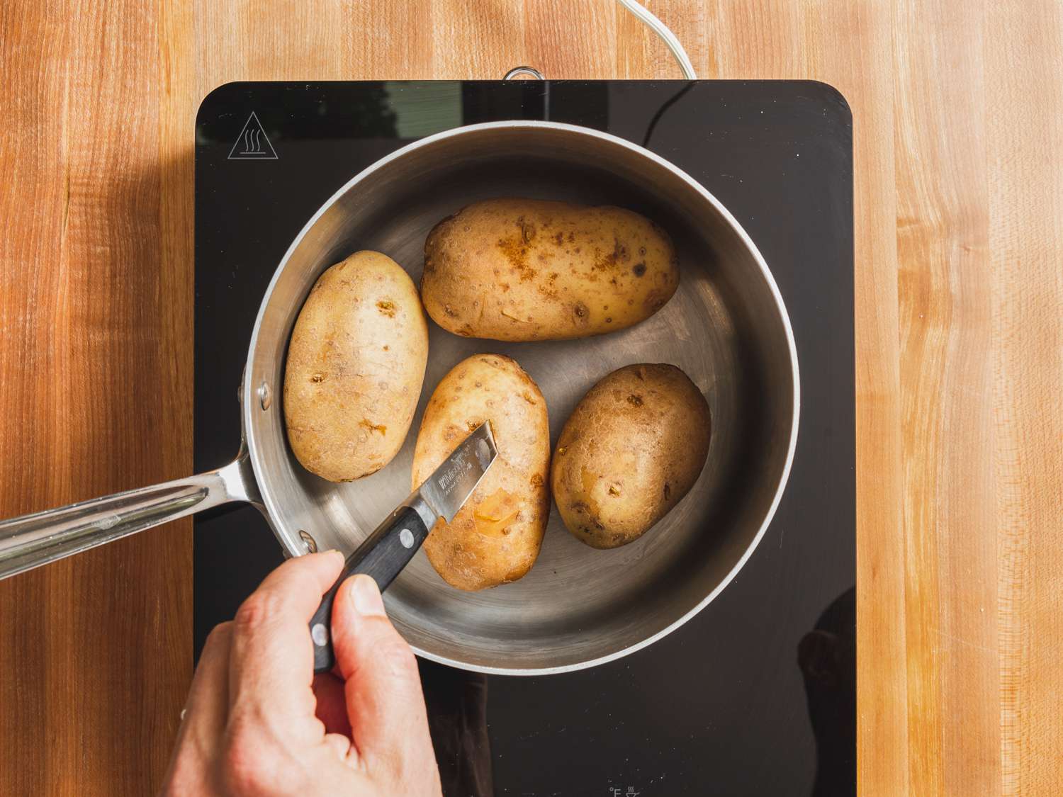 Cooked potatoes in a saucepan being tested for doneness with a sharp paring knife