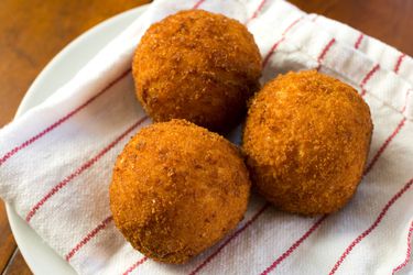 Several golden brown arancini lying on a plate lined with a patterned kitchen towel.