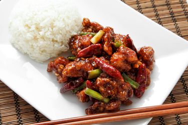Homemade General Tso's chicken on a white plate next to white rice.