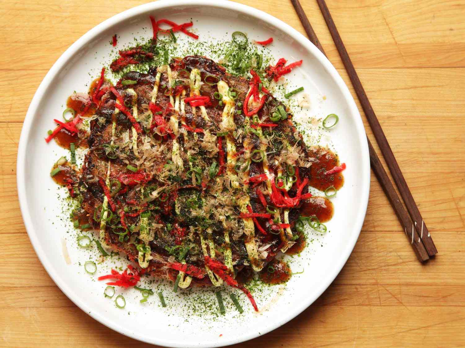 一种叫okonomiyaki的日本白菜煎饼，放在白色盘子上，旁边放着筷子。
