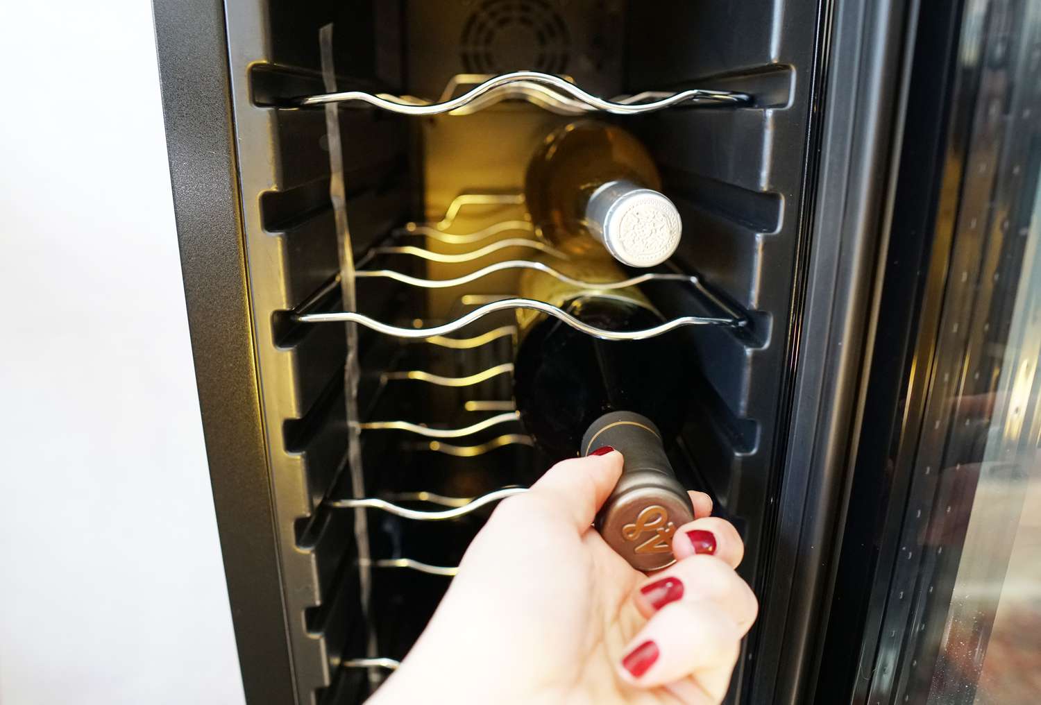a hand removing a bottle of wine from a wine fridge