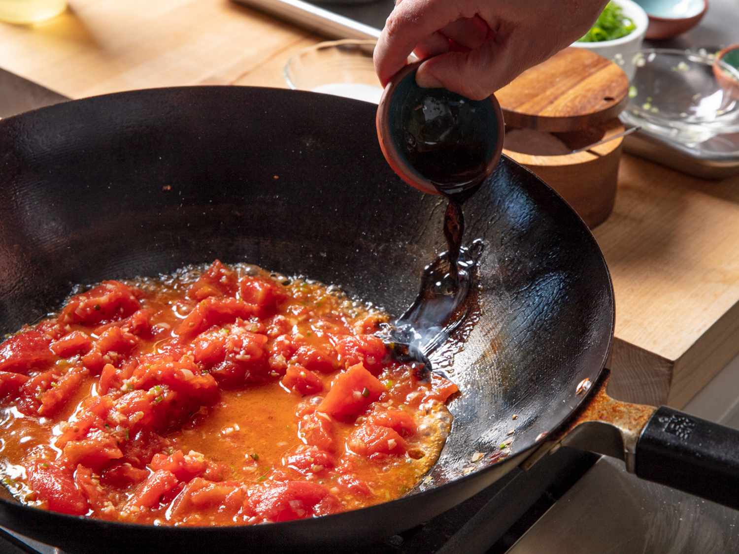 酱油被倒在锅的顶部边缘，锅里装满了西红柿。