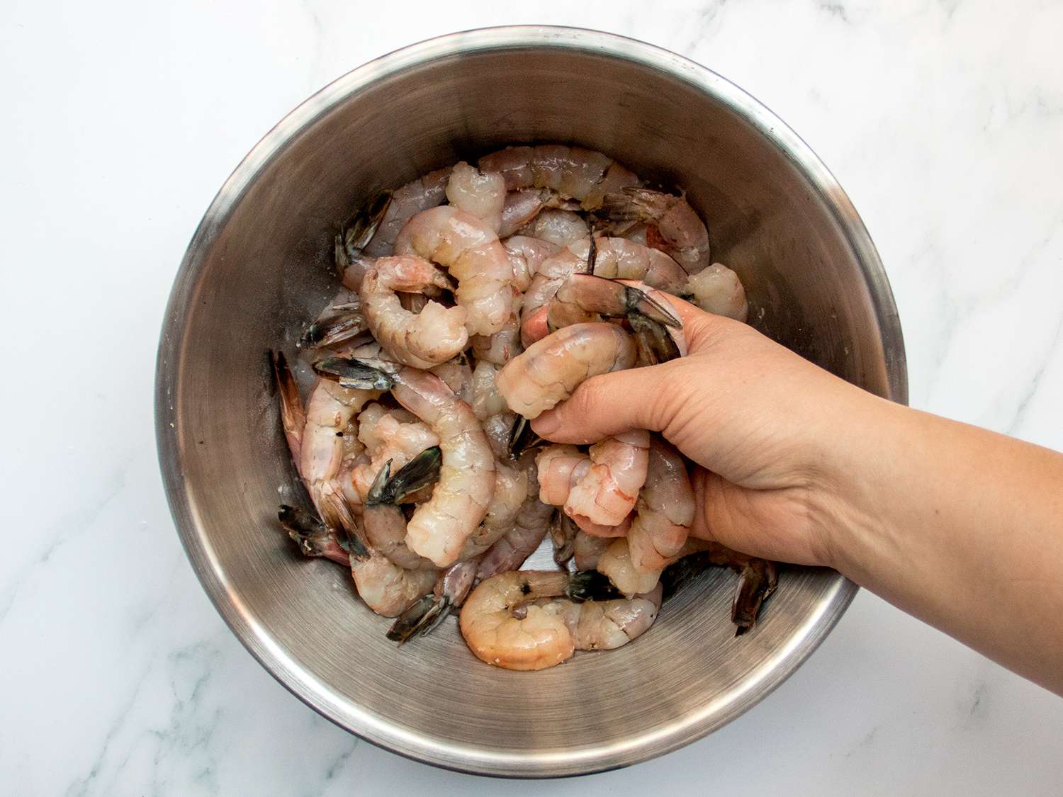 用手在金属碗里搅拌生虾。