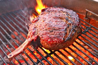 A large cowboy steak grilling on a charcoal barbecue.