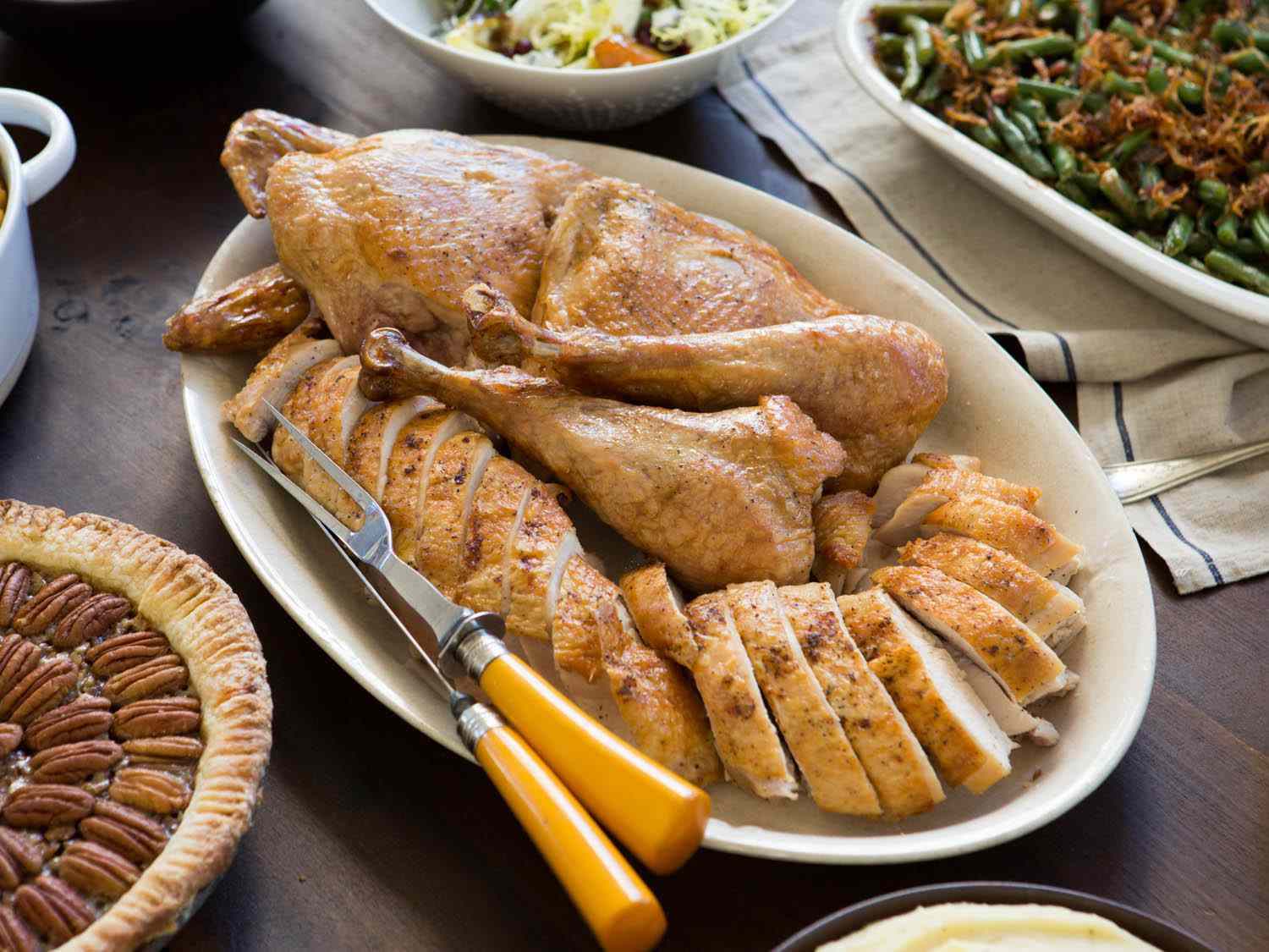 一盘用刀叉雕刻的火鸡，周围是山核桃派，青豆砂锅和沙拉