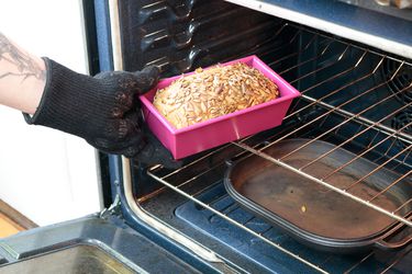 a hand taking a loaf of bread out of the oven in a pink loaf pan