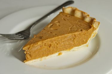 A slice of dairy-free, egg-free coconut pumpkin pie on a white plate with a fork.