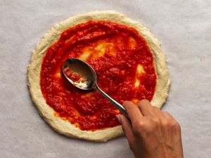 用金属勺将纽约风格的披萨酱抹在生的披萨面团上。