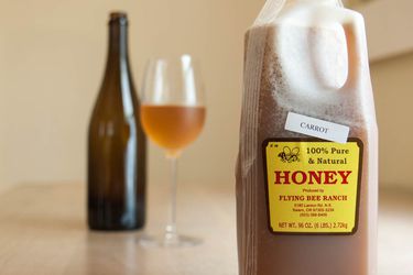 前景中有一瓶半加仑的蜂蜜，背景中有一瓶和一杯蜂蜜酒。