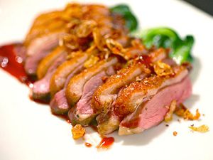 切成薄片的烤鸭胸肉放在白色盘子上，配上酱汁和sautéed绿色蔬菜。
