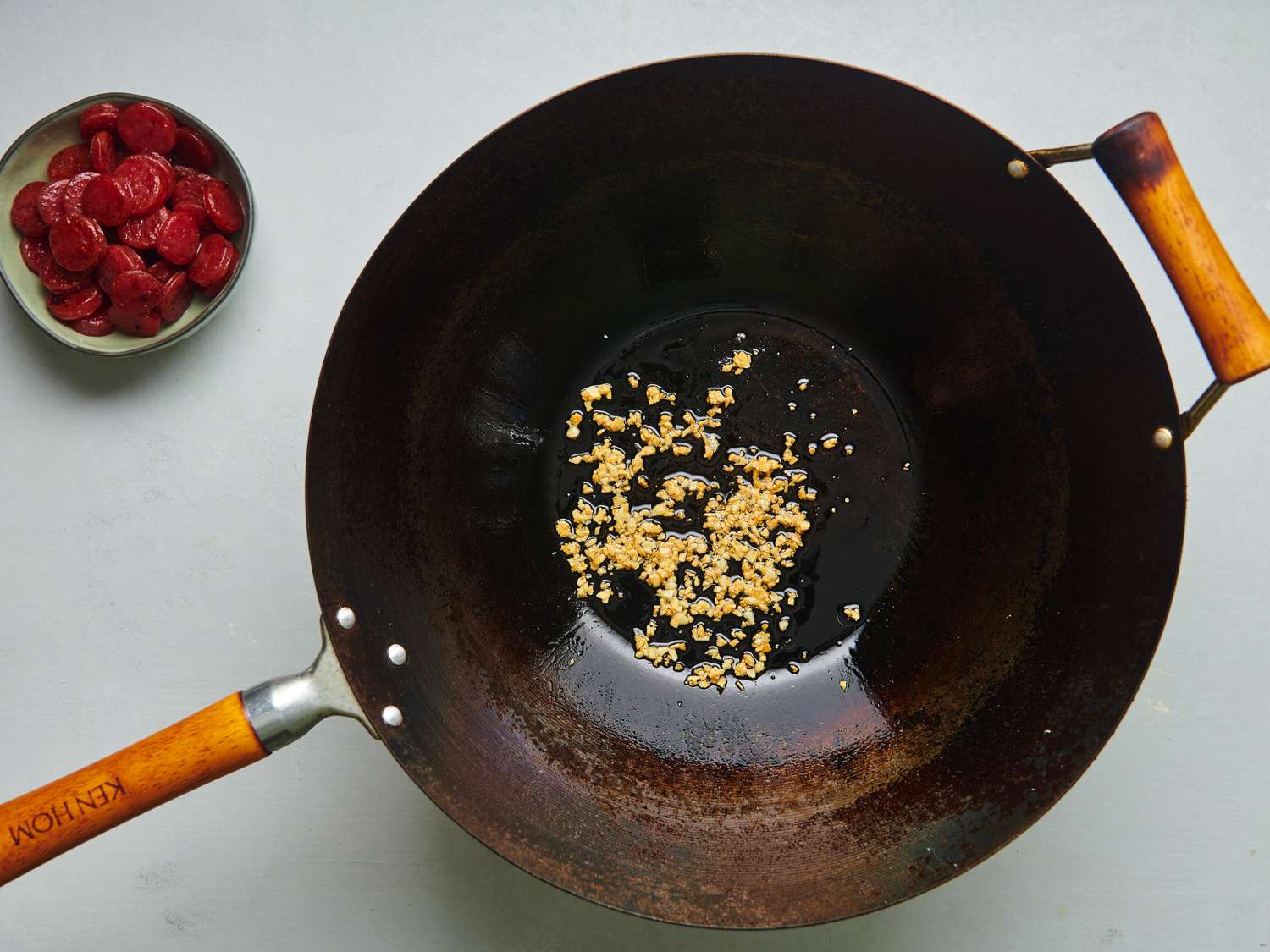 滋味的碳钢锅持有黄金大蒜和呈现褐色脂肪从中国香肠。中国炸香肠是在一个小碗在图像的左上角。