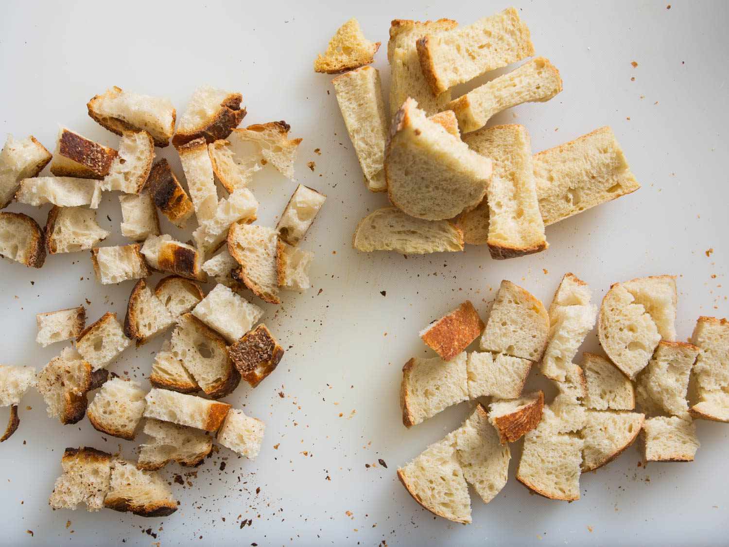 Several piles of bread cubes are arranged on a cutting surface.