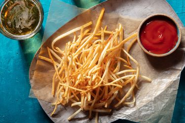 Overhead view of shoestring fries on wax paper on a platter with a ramekin of ketchup and a glass of beer alongside