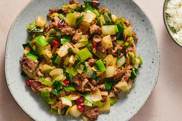 一个有斑点的陶瓷盘子里盛着一份香辣的韭菜和洋葱炒牛肉。在图片的右上角有一小碗白米饭。