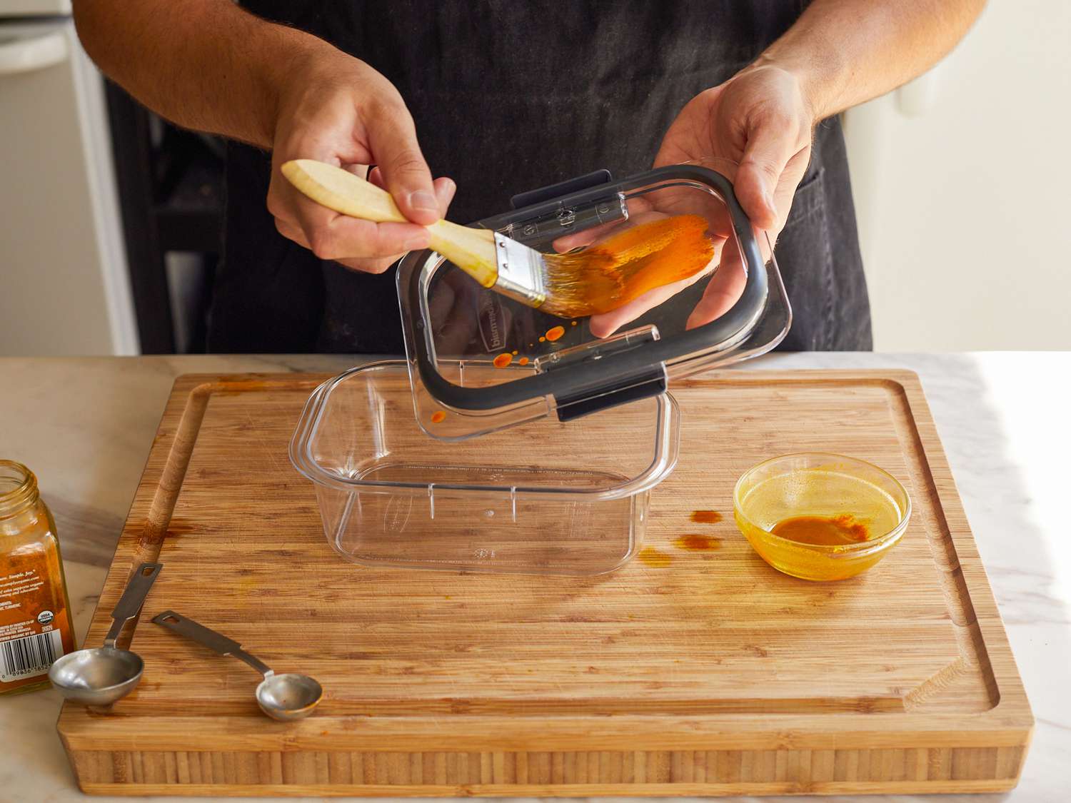 一只手用糕点刷将油和姜黄的混合物涂在食品储存容器的盖子上