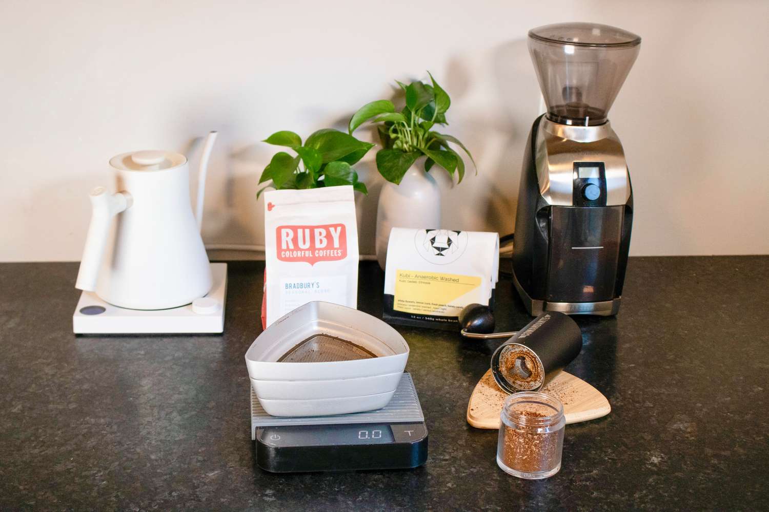 一个手持式咖啡研磨机放在咖啡筛、水壶和电动研磨机旁边