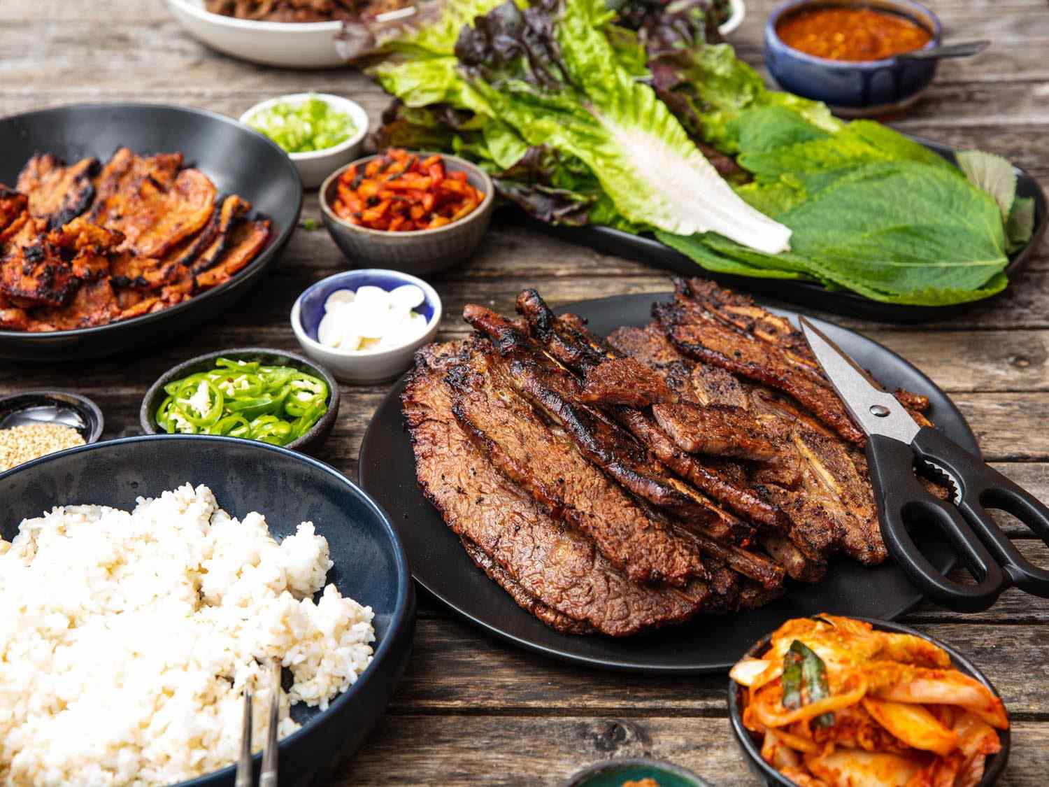 侧视图的桌子设置与韩国烧烤摊，与一盘牛肉在前景。