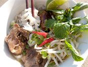 A bowl of Vietnamese pho topped with fresh herbs