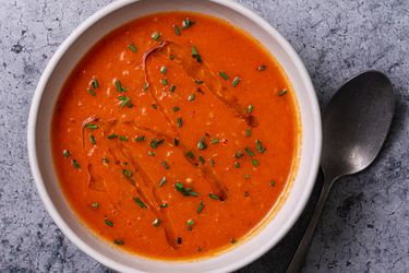 一碗奶油素食番茄汤放在石头背景上，勺子放在碗的右边。汤的表面淋上橄榄油，撒上切碎的香草。gydF4y2Ba