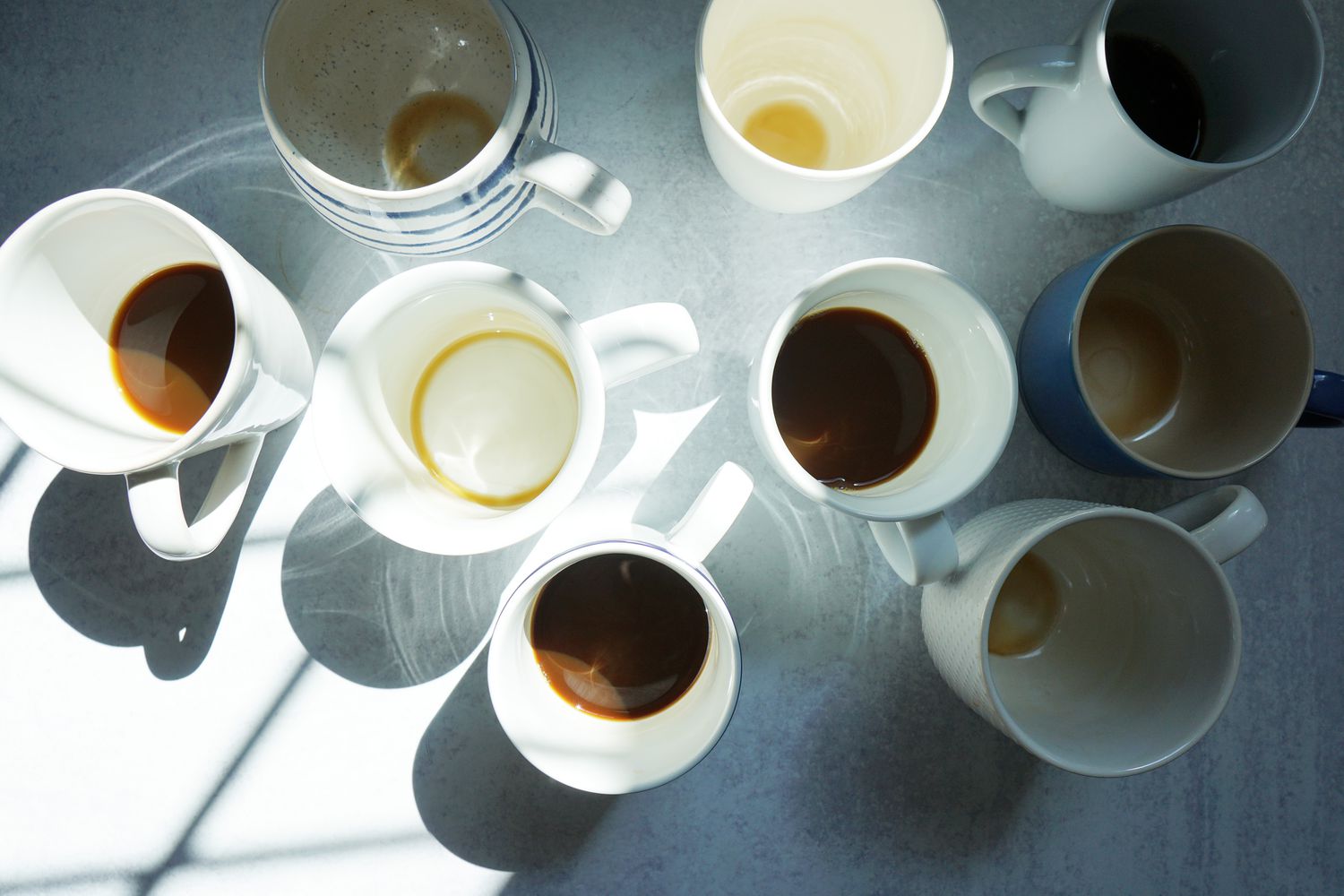 several coffee mugs on a grey surface: some half full of coffee, some empty