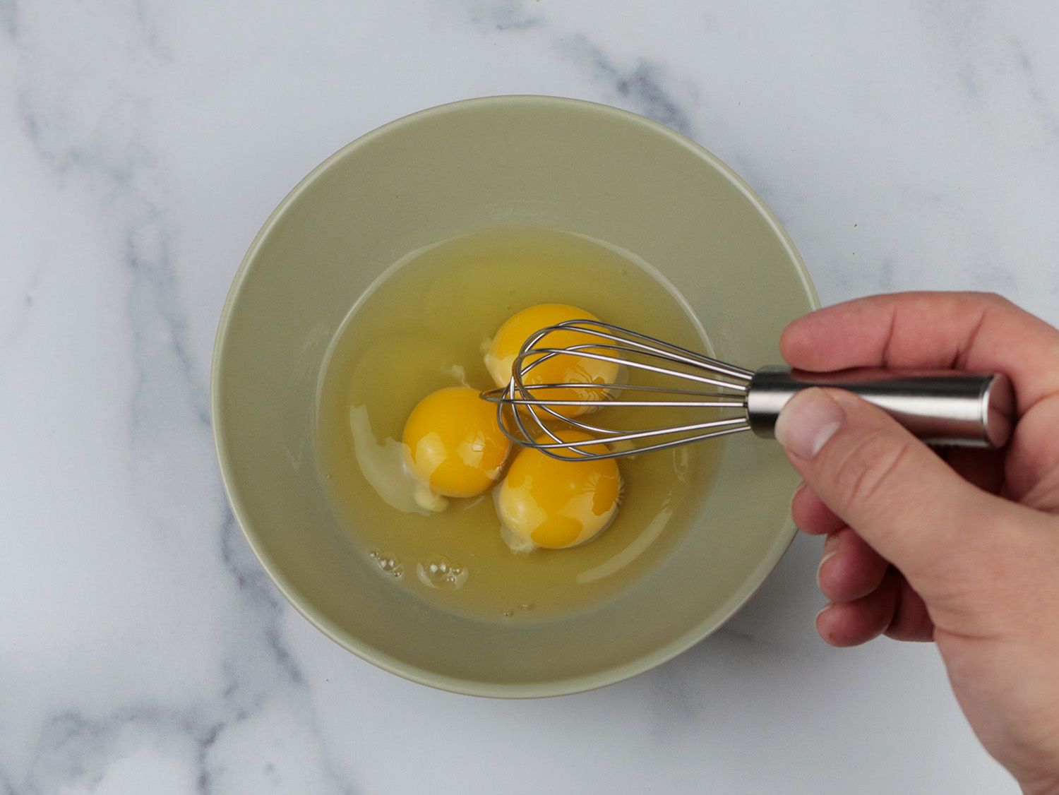 一个小型搅拌和三个鸡蛋都放在一个小碗在大理石的表面上