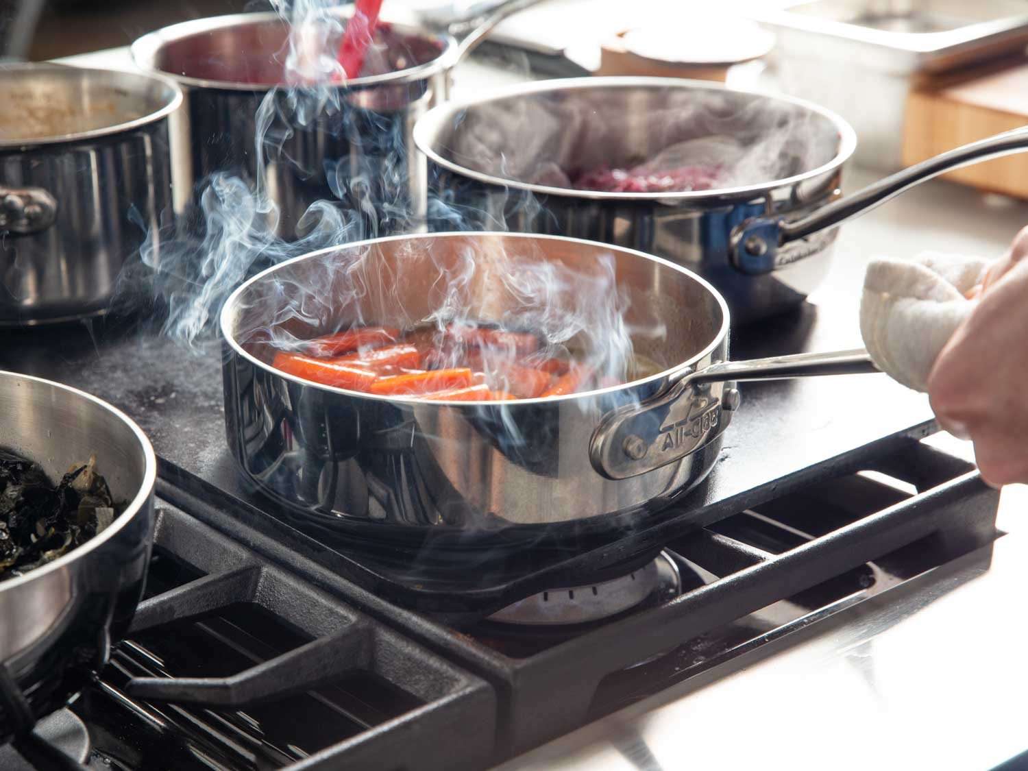 烹饪釉面胡萝卜炖锅中烤钢在煤气灶上,与其他平底锅的食物变暖在同一时间。