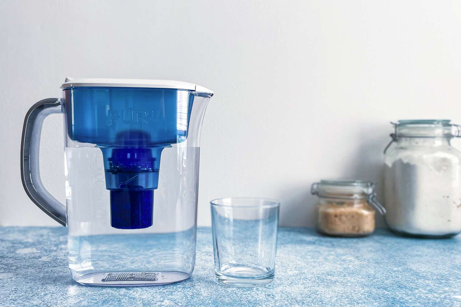 一个装满水的滤水罐放在一个空玻璃杯旁边