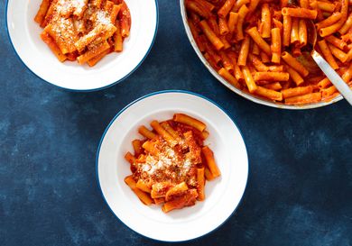 Overhead shot of two white bowls filled with pasta with tomato sauce next to pot of pasta