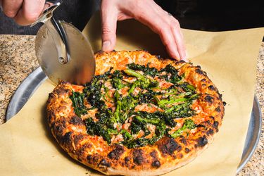 Slicing a pizza with charred broccoli rabe