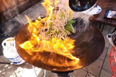 Food being tossed in wok with flames on an outdoor wok burner