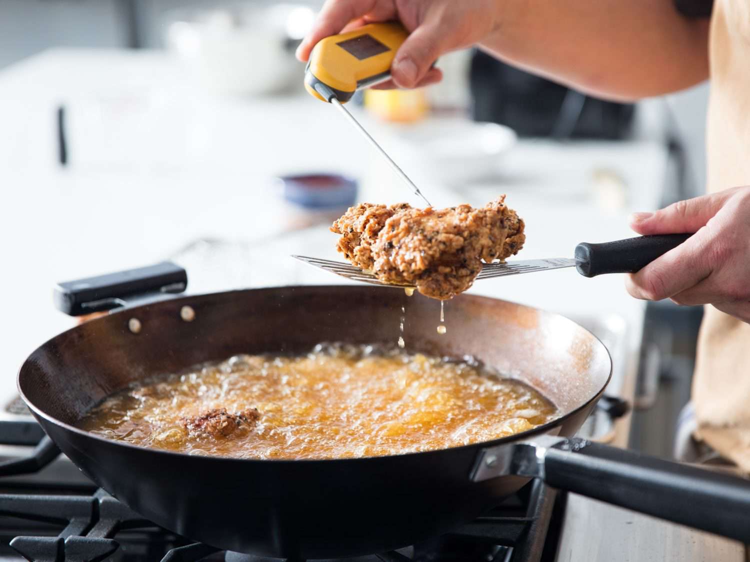 用数字温度计来测试一块炸鸡的熟度，把它高举在锅上，锅里装满了冒泡的油和更多的炸鸡块。