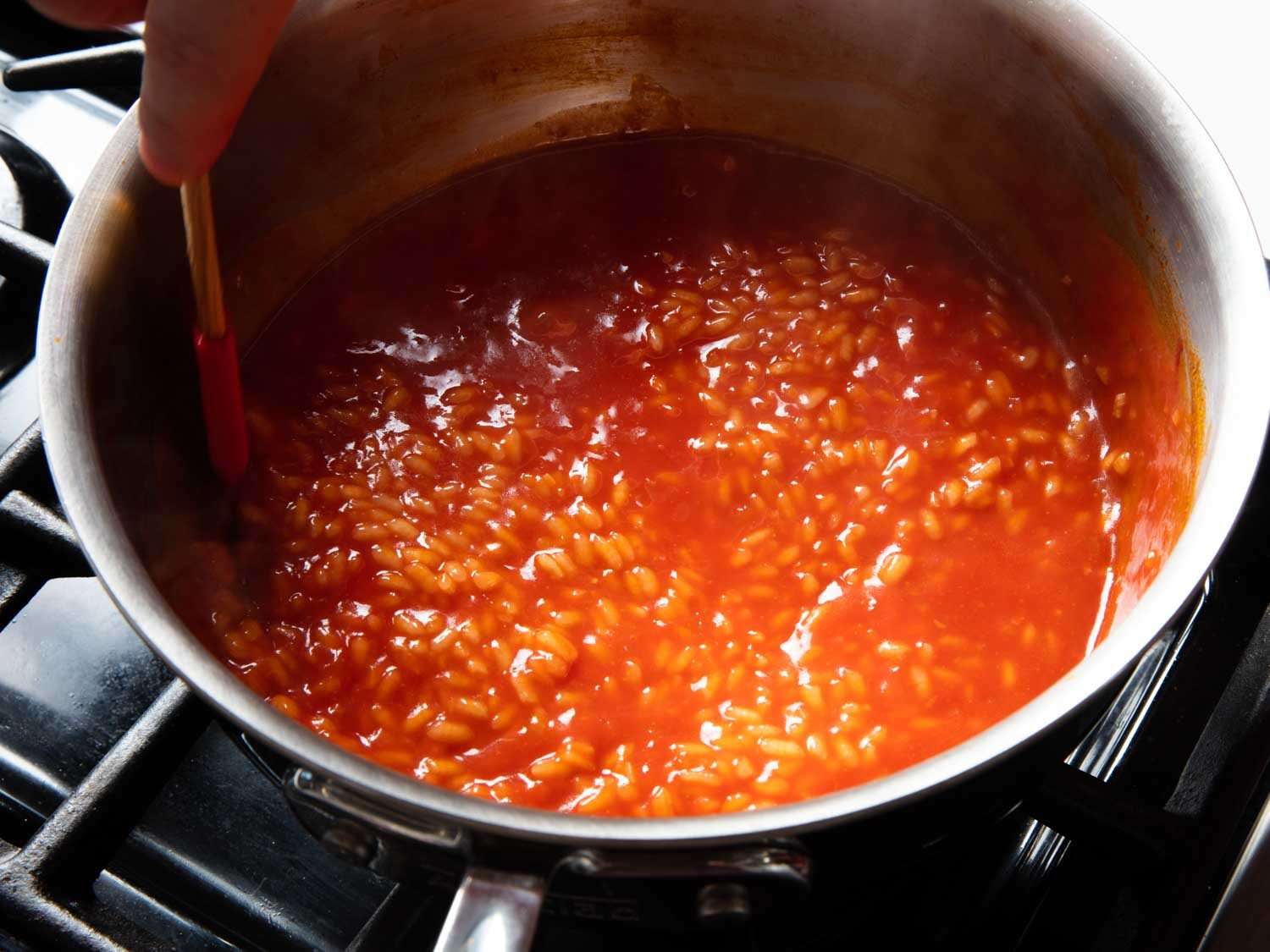 Risotto cooking with strained tomato pulp in a saucier.