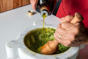 adding oil to pesto in a mortar and pestle