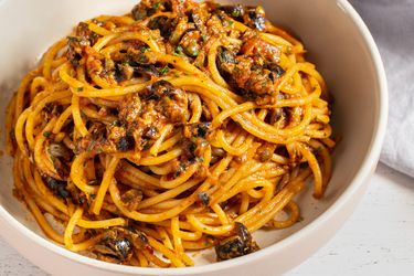 Pasta puttanesca, made with spaghetti, in a white bowl.
