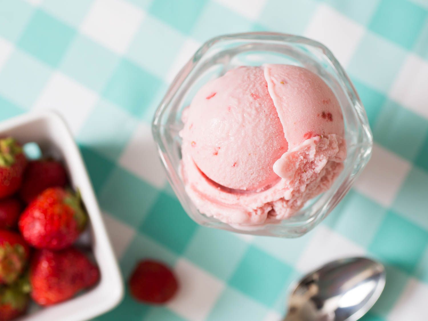 An overhead view of a scoop of strawberry ice cream next to a container of strawberries.