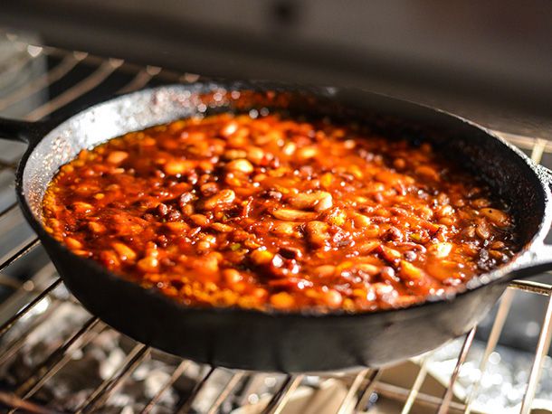 A cast iron skillet of barbecue beans placed on a rack in an oven, ready to finish cooking.